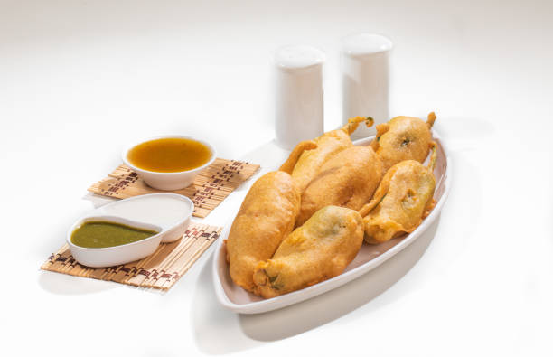 A plate of crispy Mirchi Vada, showcasing stuffed green chilies, golden brown in color, served with mint and tamarind chutneys.