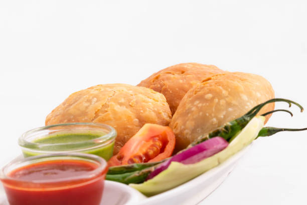 A close-up of golden-brown Pyaaj Kachori, filled with spiced onions, served with chutneys on a traditional plate.