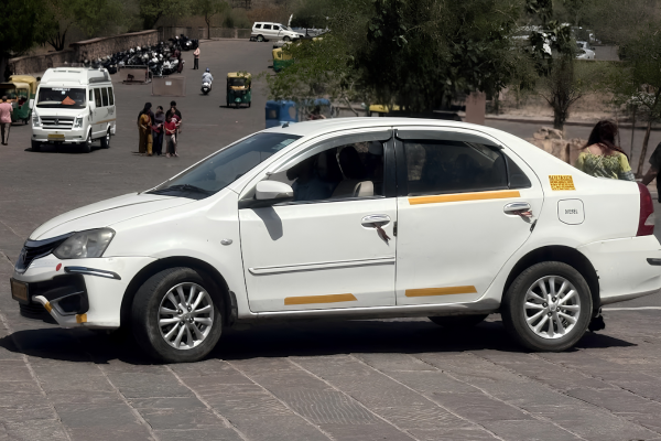 White sedan taxi parked at a tourist attraction in Jodhpur, Rajasthan, offering local sightseeing and private cab services.
