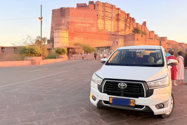 White Toyota Innova parked near Mehrangarh Fort in Jodhpur during sunset, showcasing private cab service for Rajasthan sightseeing tours.