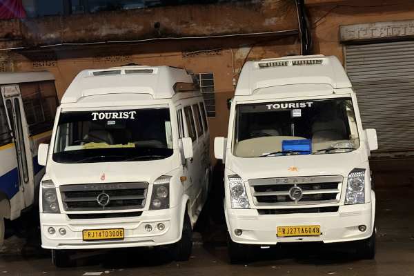 Two white Tempo Traveller tourist vehicles parked outside a building.