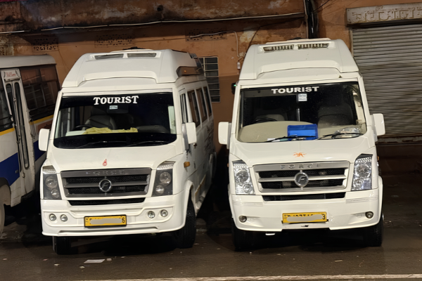 Two white tourist Tempo Traveller vehicles parked side by side.